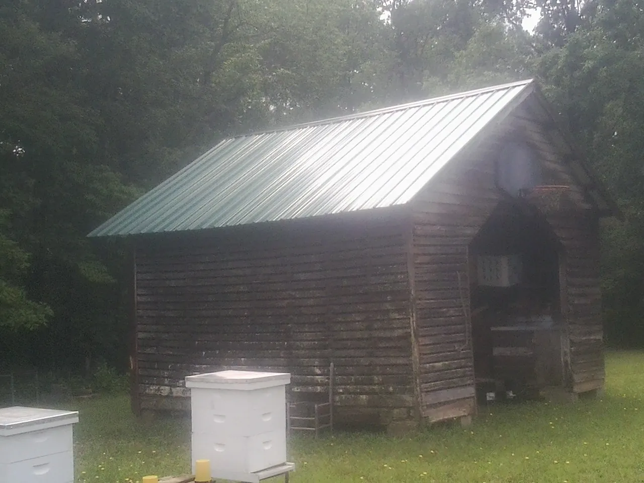 Green metal roof on a weathered barn beside stacked beehives in Macedonia