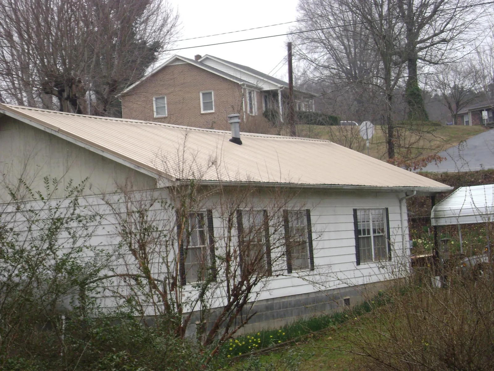 Tan metal roof on a white sided house set into a hillside — Commercial Roofing by Roofing Brothers in Macedonia